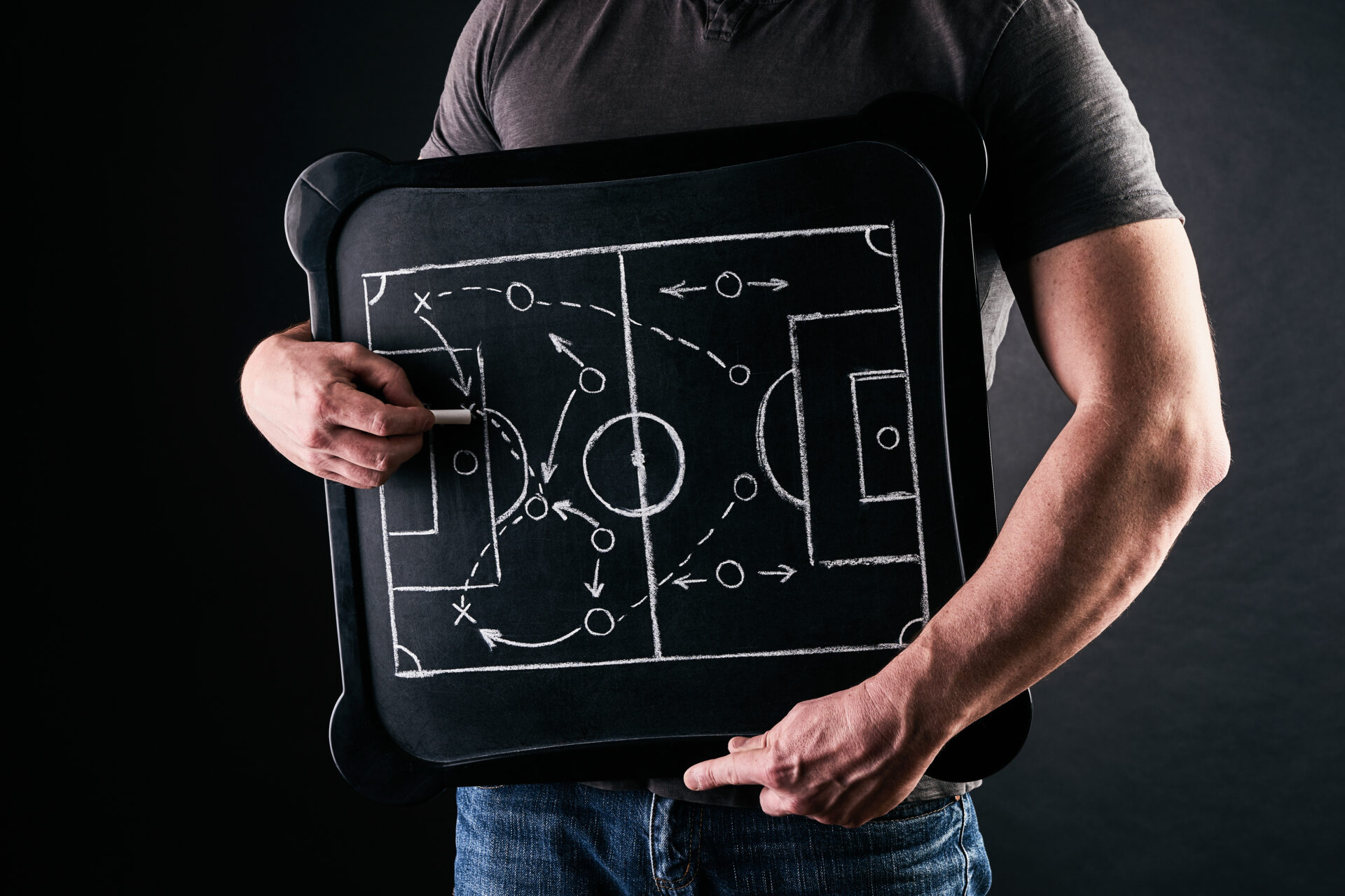 Hand of a football or soccer play coach drawing a tactics of football game with white chalk on blackboard at changing room during the time out